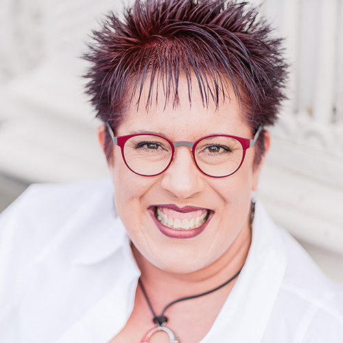 Tami Levin in a smart blazer smiling with a house plant in the background